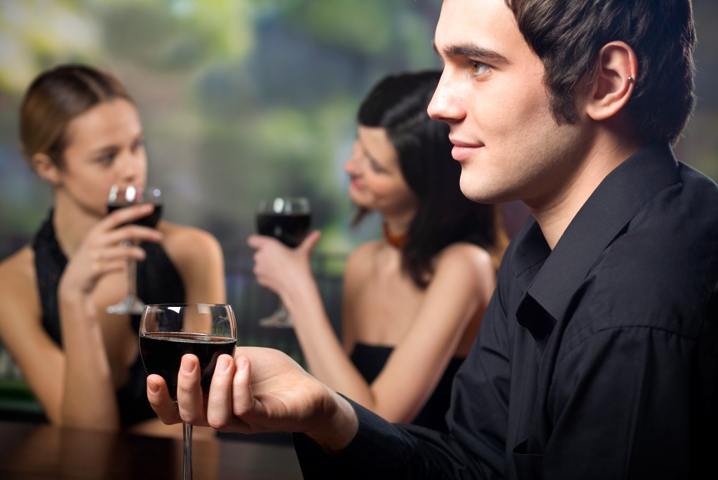 Young man with glass of red-wine and two women